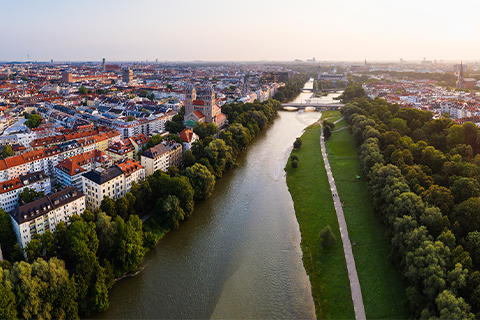 Aerial view of Munich with a river, trees, and a walking path alongside the river.